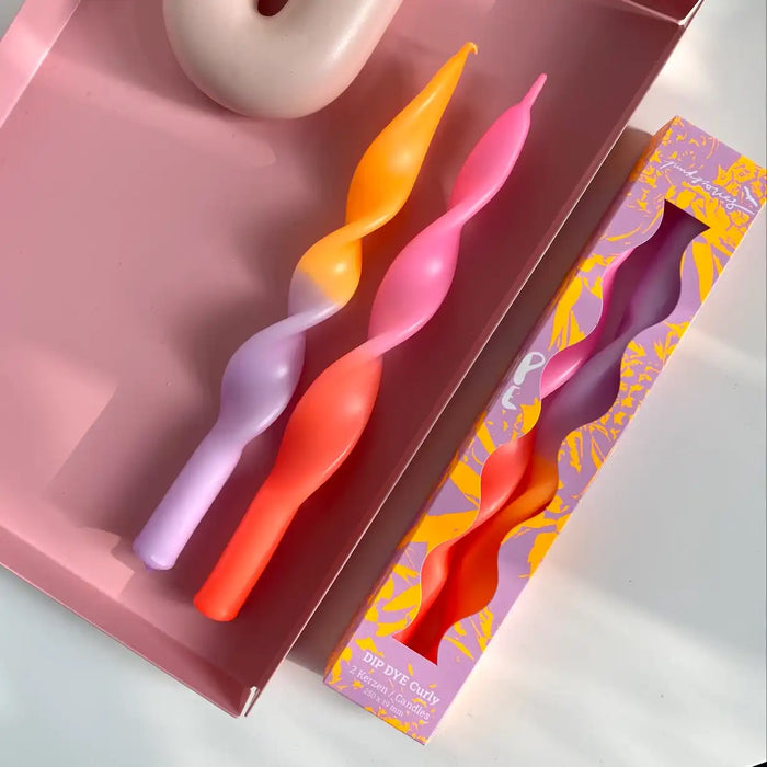 2--gedrehte-Stabkerzen-Dip-Dye-Curly-Miami-Edition-lila-vor-Lila-Hintergrund-mit-Verpackung-in-einer-schale